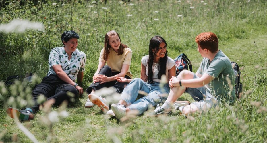 Four students sitting on grass in the sunshine