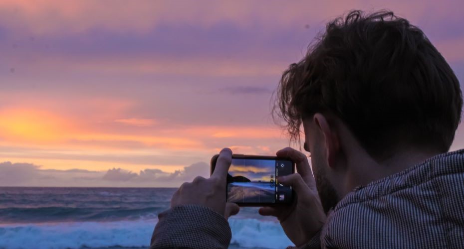 Student taking a photo of the sunset over the sea