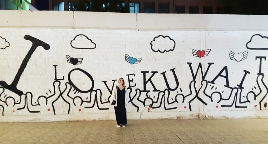 Student standing in front of a mural which reads 'I love Kuwait'