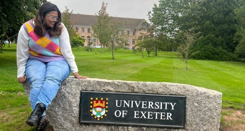 Student sat on a rock with the University of Exeter sign