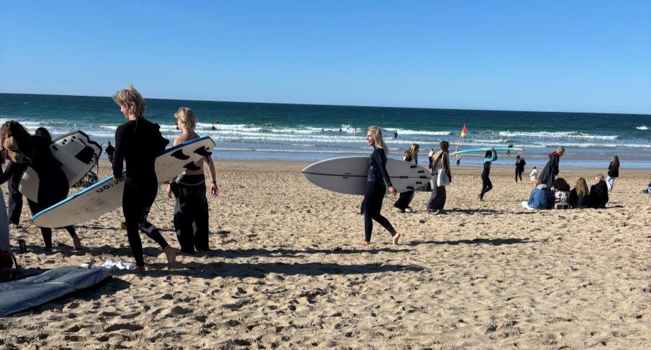 Students in wetsuits with surfboards on a sunny beach