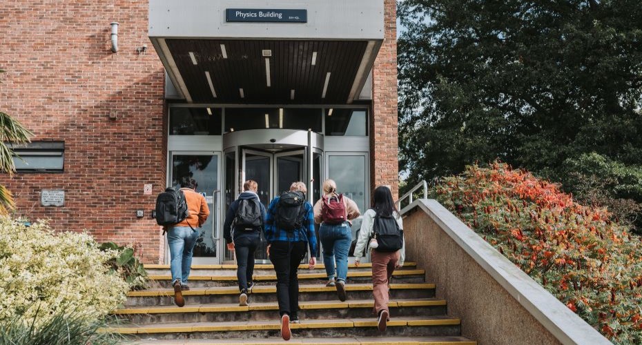 Group of students walking away from the camera up the steps to the Streatham Campus physics building