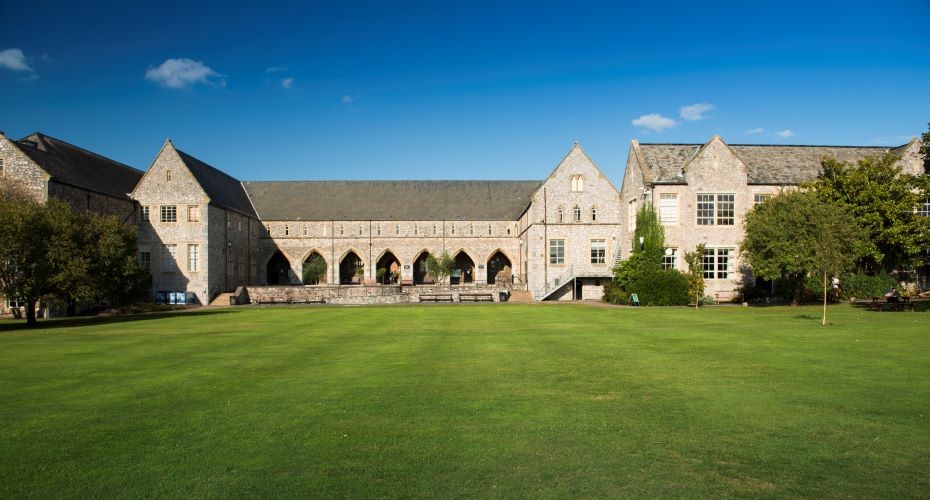 Large, historic stone building behind a well-kept grass lawn