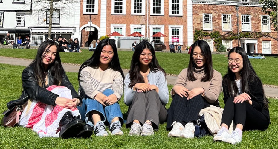 A group of female students sat together on a grass lawn