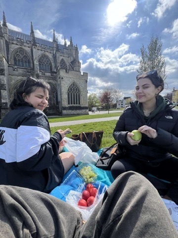 Photo of students enjoying the sunshine on the grass outside Exeter cathedral