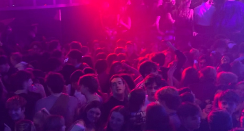 Crowded room of students dancing. Strobe lights shine pink and purple over the dancers.