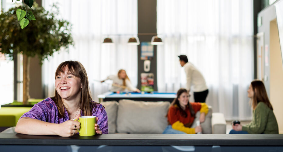 Smiling student holding a yellow mug in the common area of student accommodation