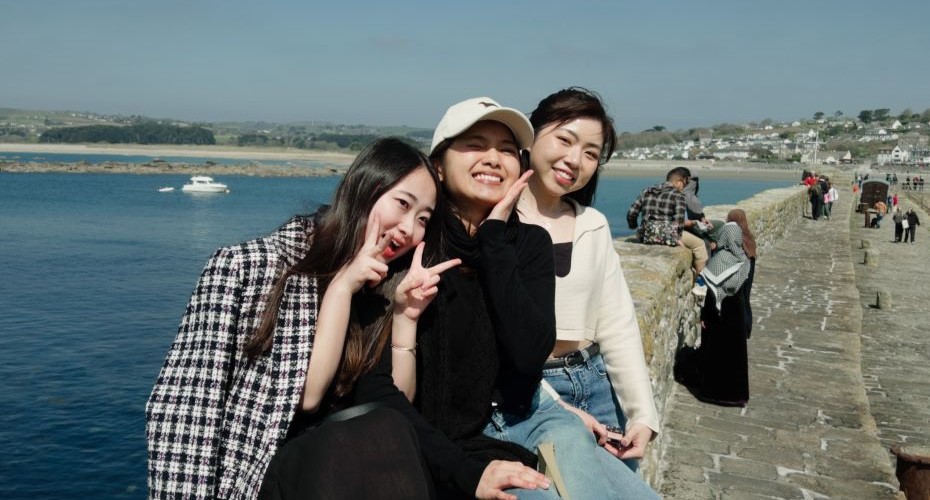 Three female students posing for the camera in front of a sunny beach