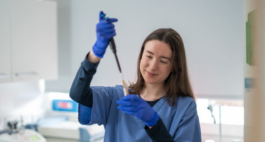 Caitlyn in medical scrubs with a piper and test tube in a lab